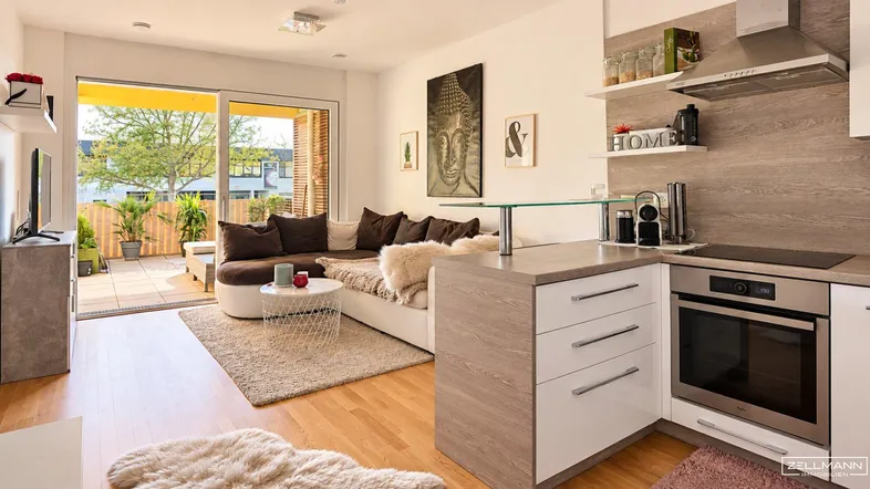 Heller offener Wohnbereich mit integrierter Küche, Holzboden und Zugang zur Terrasse.