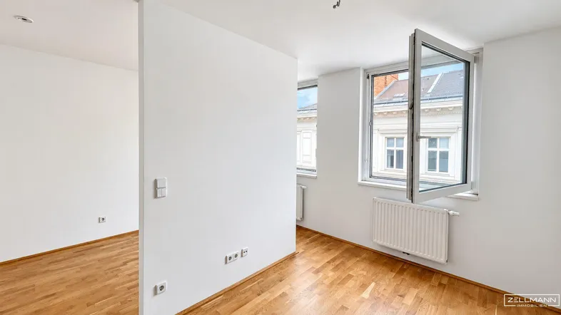 Helles Zimmer mit Holzboden, weißen Wänden und einem Fenster mit Blick auf die Umgebung.