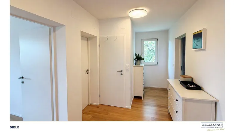 Heller Flur mit Holzfußboden, weißer Kommode und einem Fenster, das Tageslicht hereinlässt.