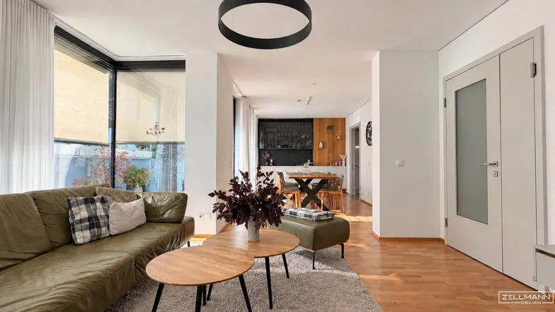 Helles Wohnzimmer mit bequemer Couch, Holzboden und Blick in den Essbereich und die Küche.