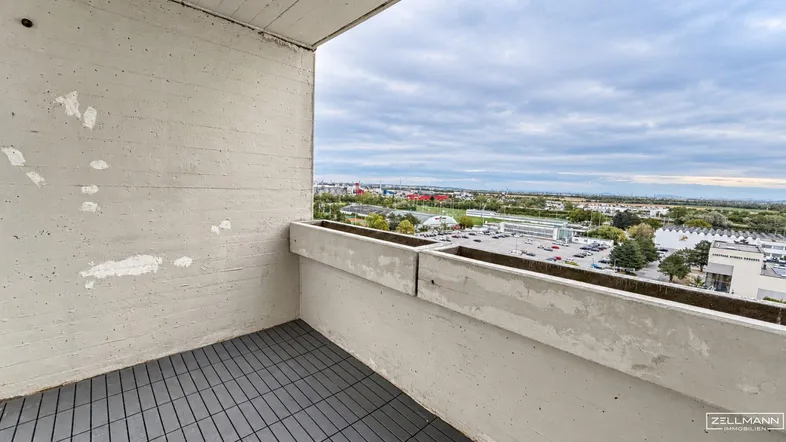 Geräumiger Balkon mit Betonwänden und Blick auf die Stadt sowie die umliegende Landschaft.