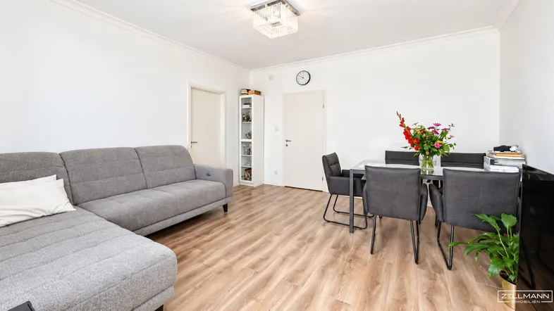 Helles Wohn- und Esszimmer mit grauem Ecksofa, Esstisch und Laminatboden.