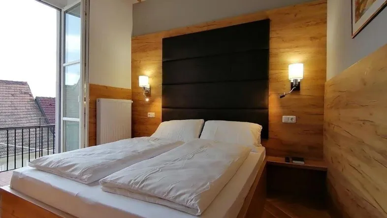 Helles Schlafzimmer mit Holzbett, gepolstertem Kopfteil und Zugang zu einem kleinen Balkon.