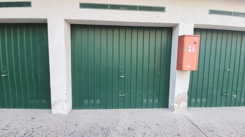 Außenansicht einer Reihe von Garagen mit grünen Toren und einem roten Kasten an der Wand.