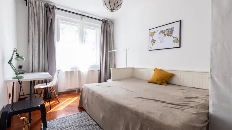 Helles Schlafzimmer mit Einzelbett, Schreibtisch und großem Fenster mit Vorhängen.