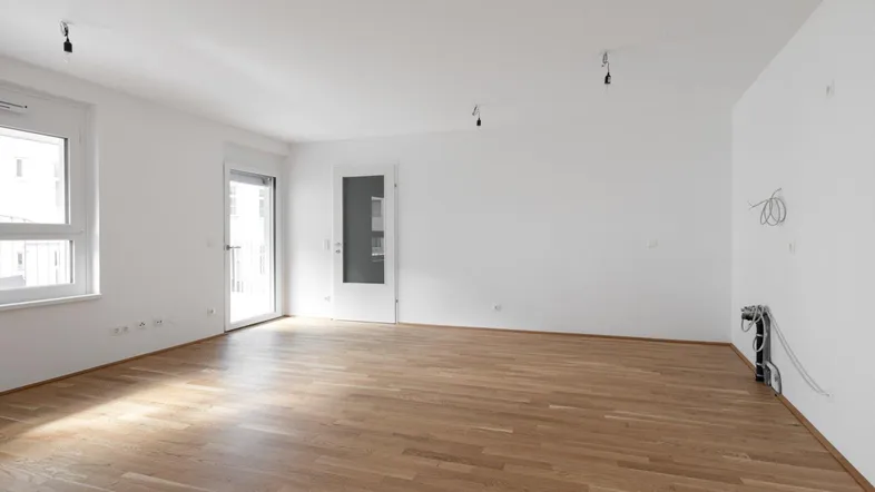 Heller, leerer Raum mit Parkettboden, weißen Wänden und Zugang zu einem Außenbereich.