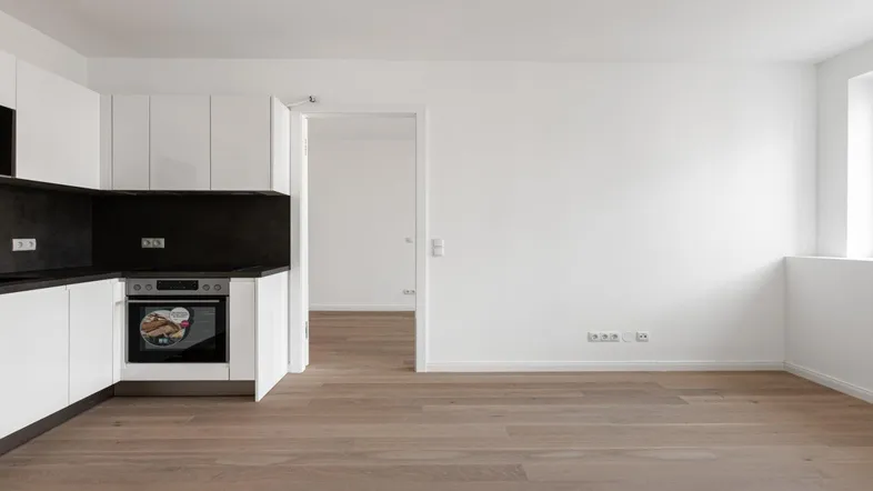 Moderne, helle Küche mit weißen Schränken, dunkler Arbeitsplatte und integriertem Backofen.
