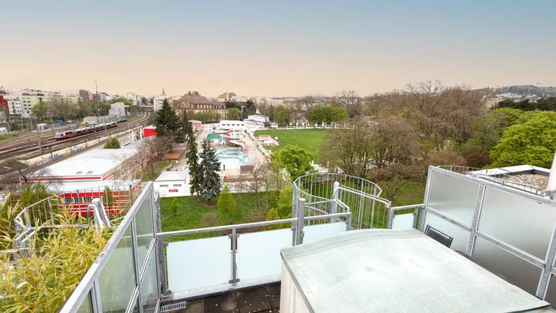 Geräumige Dachterrasse mit Sitzgelegenheiten und weitem Blick über die Stadt und ein Freibad.