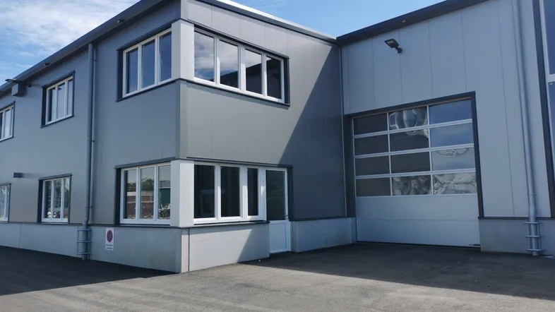 Modernes Geschäftsgebäude mit grauer Fassade, großen Fenstern und einem großen Rolltor.