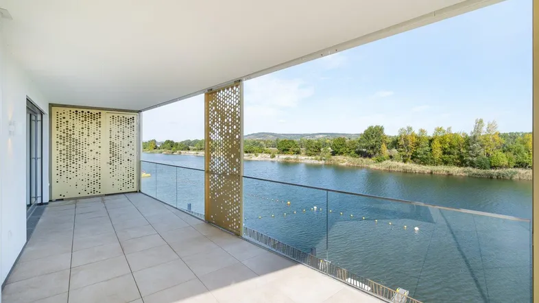 Geräumiger Balkon mit Fliesenboden, Glasbrüstung und weitem Blick auf den See und die grüne Umgebung.