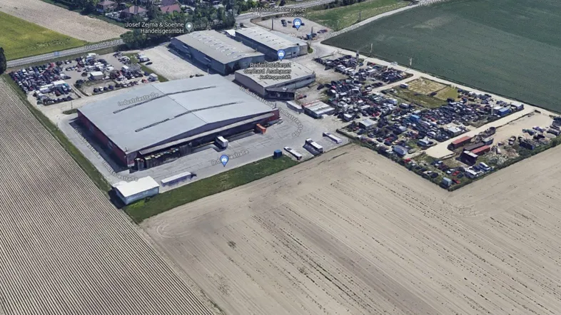 Luftaufnahme eines Industriegebiets mit großen Hallen, Parkplätzen und umliegenden Feldern.