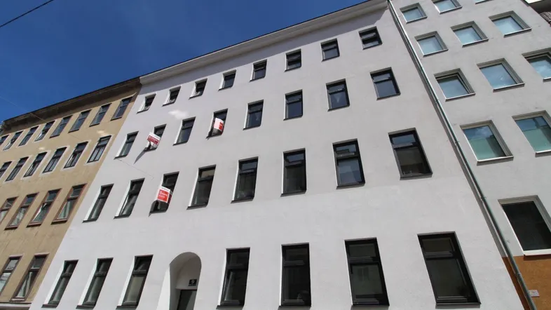 Die frisch renovierte Fassade eines Altbaus mit vielen Fenstern unter blauem Himmel.
