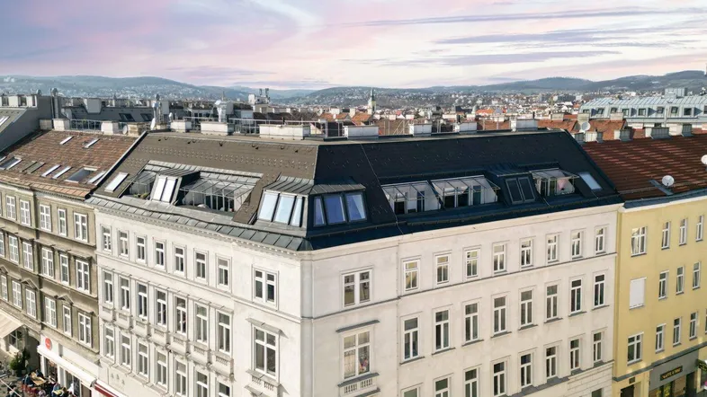 Luftaufnahme eines Eckgebäudes in der Stadt mit Mansarddach und Blick über die Dächer Wiens.