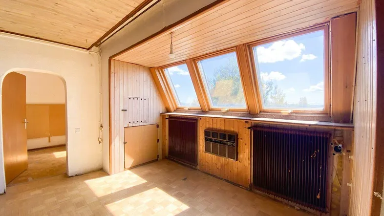 Heller Raum mit Holzdecke und -wänden, Parkettboden und großen Dachfenstern, die viel Licht hereinlassen.