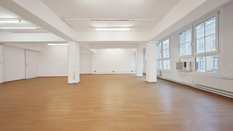 Großer, heller Büroraum mit Holzboden, vielen Fenstern und sichtbaren Deckenbalken.