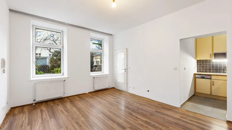 Helles Wohnzimmer mit Holzboden und Blick ins Grüne, angrenzend an eine kleine Küche.