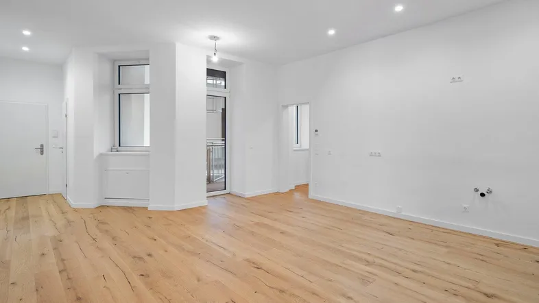 Helles, leeres Wohnzimmer mit neuem Parkettboden und Zugang zu einem kleinen Balkon.
