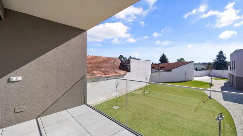 Moderner Balkon mit Glasgeländer und Fliesenboden, bietet Blick auf den Gartenbereich.