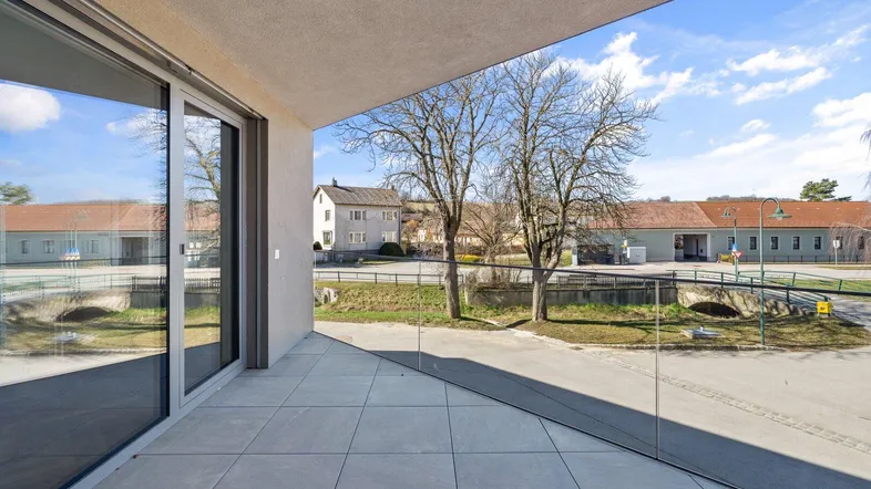 Geräumige Terrasse mit Fliesenboden und Glasgeländer, bietet einen weiten Blick auf die Umgebung.