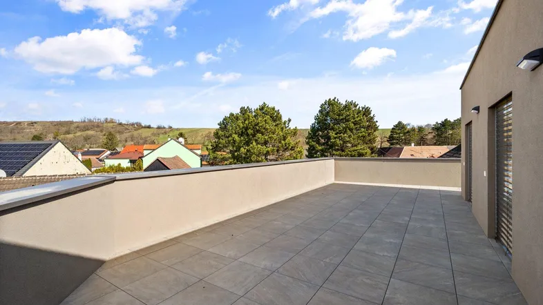 Weitläufige Dachterrasse mit Fliesenboden und Panoramablick über die grüne Umgebung.
