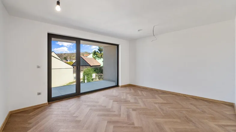 Helles, leeres Zimmer mit modernem Fischgrätparkett und Zugang zu einem Balkon mit Blick auf die Umgebung.