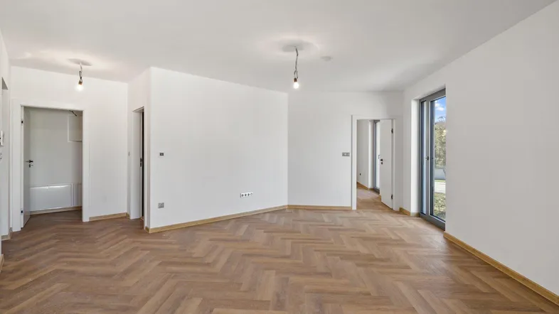 Helles, leeres Zimmer mit Fischgrätparkett und Zugang zu weiteren Räumen sowie einem Balkon.