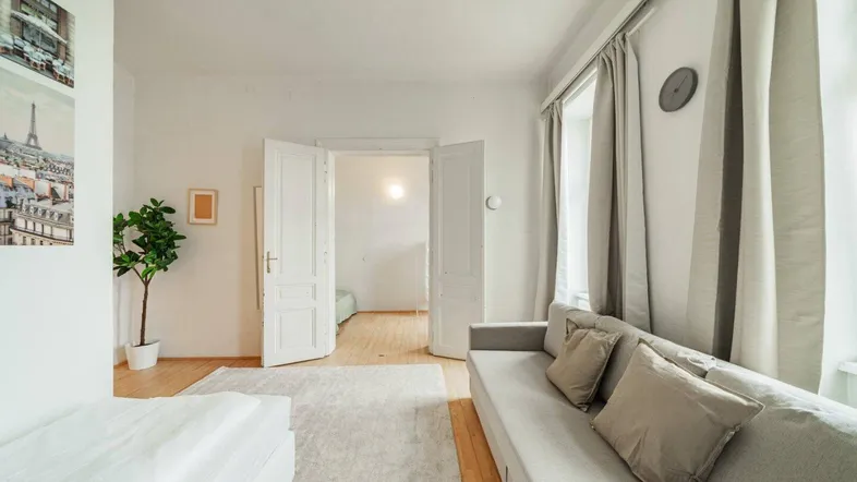 Geräumiger Wohnbereich mit Holzboden, hellem Teppich und Doppeltüren zu einem weiteren Zimmer.