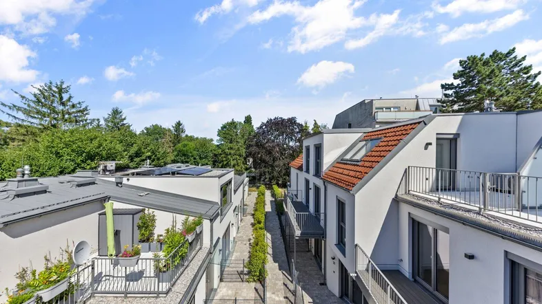 Moderne Wohnanlage mit mehreren Gebäuden, Balkonen, Terrassen und begrünten Außenbereichen unter blauem Himmel.
