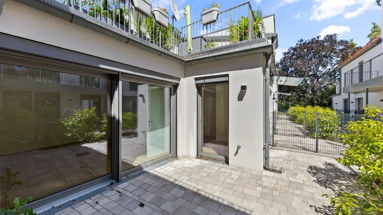 Gepflasterte Terrasse mit Zugang zu den Innenräumen und Blick auf die begrünte Umgebung.