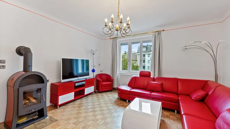 Helles Wohnzimmer mit rotem Ledersofa, Kaminofen und Parkettboden.