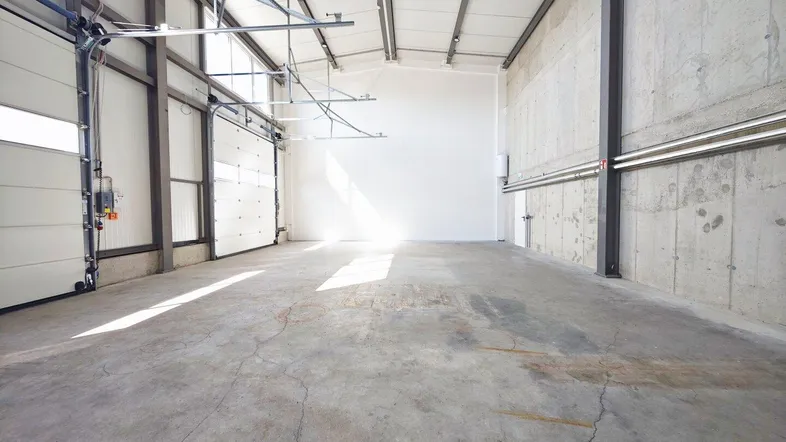 Geräumige Lagerhalle mit hohen Decken, Betonboden und großen Rolltoren für den Zugang.