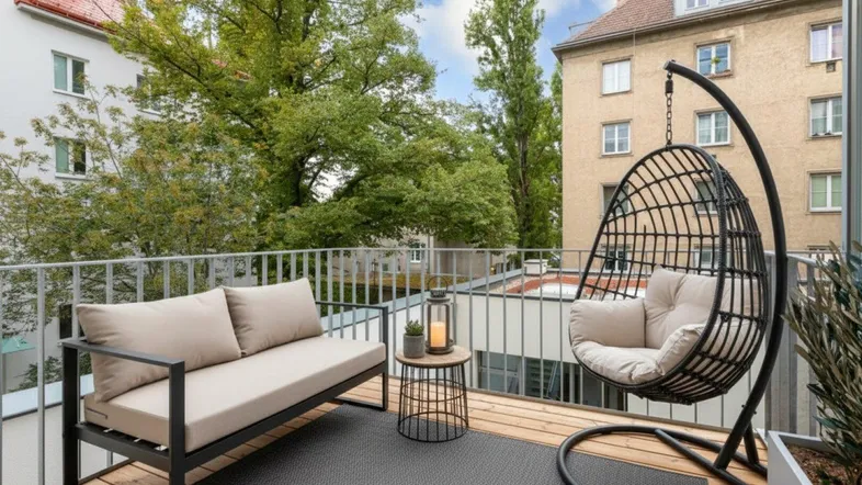 Moderner Balkon mit bequemen Outdoor-Möbeln und Blick auf grüne Bäume und umliegende Gebäude.
