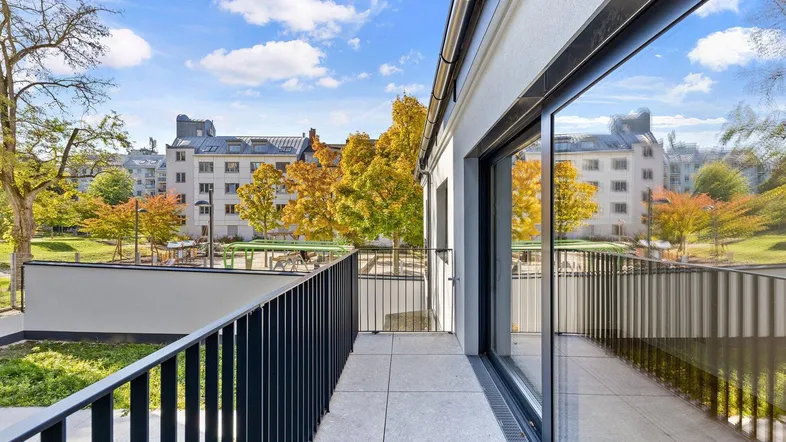 Geräumige Terrasse mit modernem Geländer und Blick auf grüne Bäume und umliegende Gebäude.