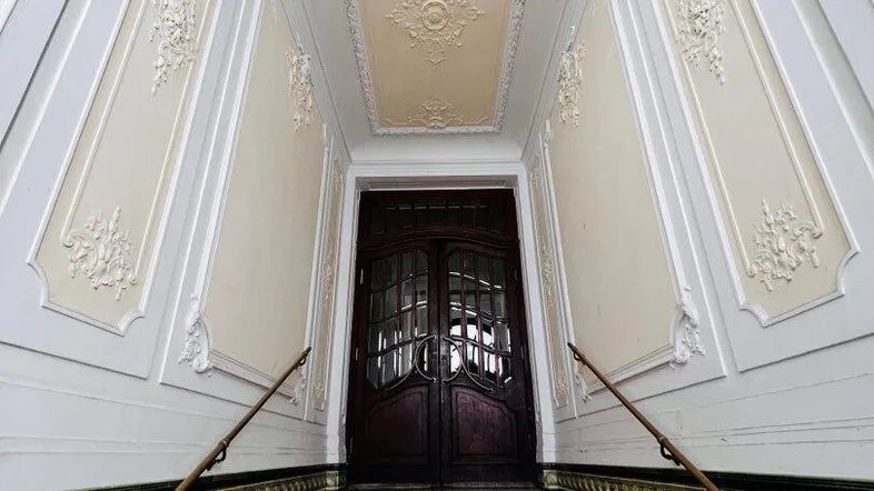 Eindrucksvolles Treppenhaus mit Stuckverzierungen, kunstvollen Fliesen und einer eleganten Holztür.