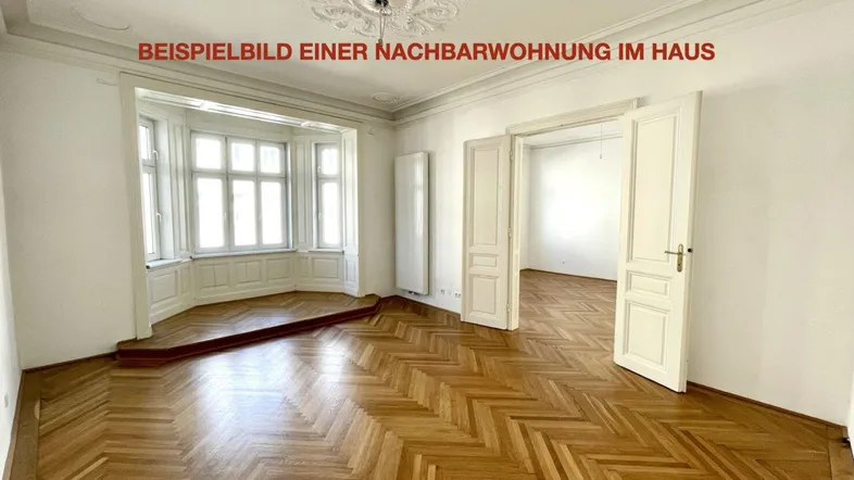 Helles Zimmer mit Fischgrätparkett, Stuckdecke und einem schönen Erkerfenster, typisch für Altbauten.