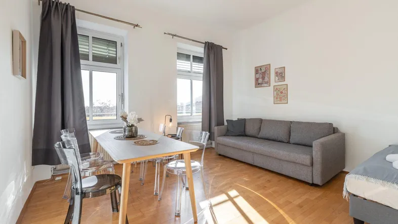 Helles Wohn- und Esszimmer mit Parkettboden, bequemer Couch und modernem Esstisch.