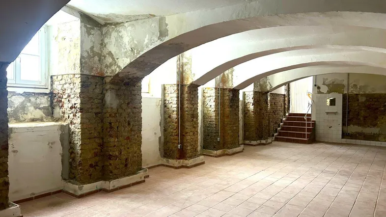 Großer Kellerraum mit Gewölbedecke, Fliesenboden und sichtbaren Ziegelpfeilern, der renovierungsbedürftig ist.