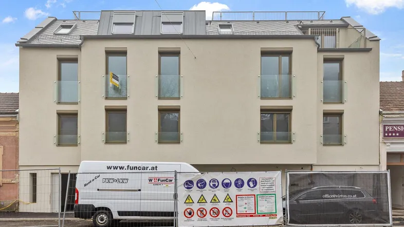 Moderne Gebäudefassade im Bauzustand mit Bauzaun und Lieferwagen davor.