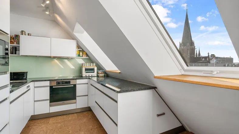 Moderne Küche im Dachgeschoss mit weißen Schränken, Granitarbeitsplatte und Blick auf die Stadt.