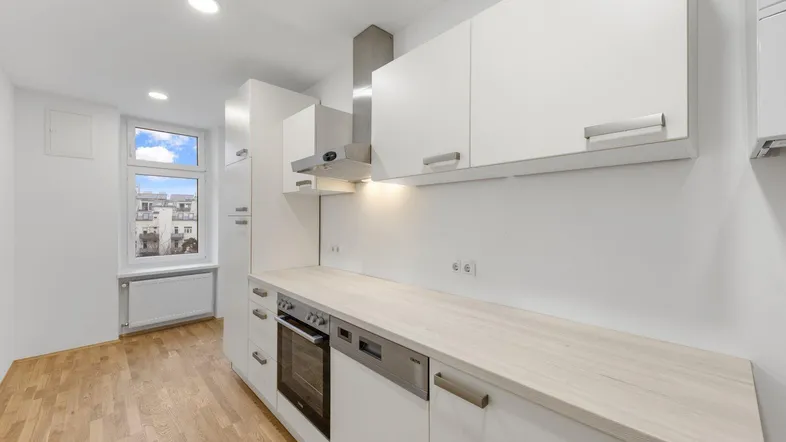 Moderne Einbauküche mit weißen Hochglanzfronten, Holz-Arbeitsplatte und Blick aus dem Fenster.