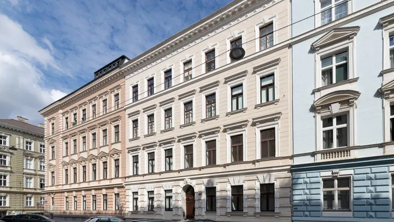 Historisches Gebäude mit traditioneller Fassade und parkenden Autos auf der Straße unter blauem Himmel.