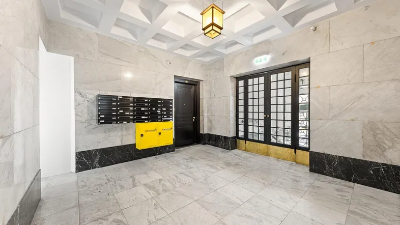 Elegantes Entrée mit Marmorwänden, Fliesenboden und dekorativer Deckenbeleuchtung.