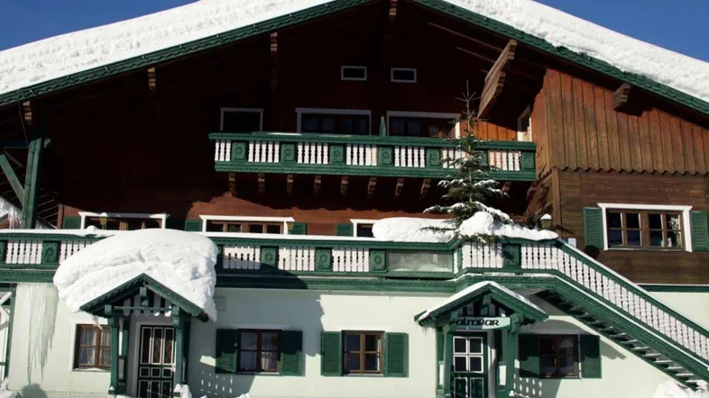 Traditionelles alpines Gebäude mit Holzbalkonen und schneebedecktem Dach in winterlicher Landschaft.