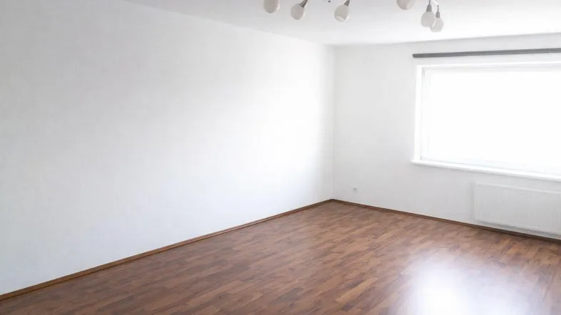 Geräumiges Zimmer mit Laminatboden, Heizkörper und Deckenleuchte, ideal für Wohnzwecke.