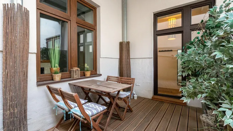 Helle Terrasse mit Holzboden, Sitzgelegenheiten und Blick auf die umliegenden Gebäude.