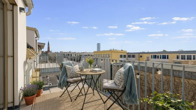 Möblierter Balkon mit Teppich und Lichterkette, bietet einen weiten Blick über die Stadt.