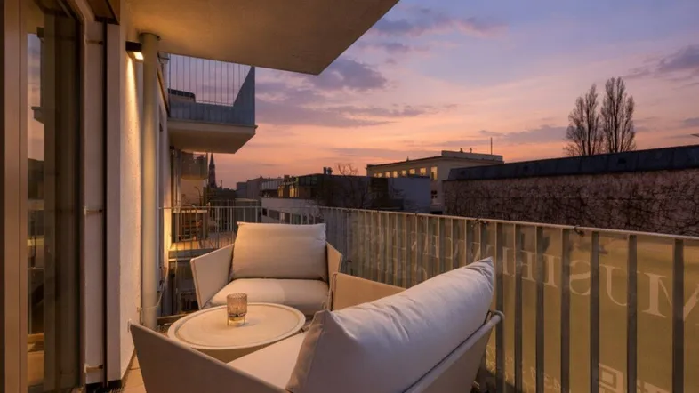 Gemütlicher Balkon mit Sitzgelegenheiten und Blick auf die Stadt bei Sonnenuntergang.