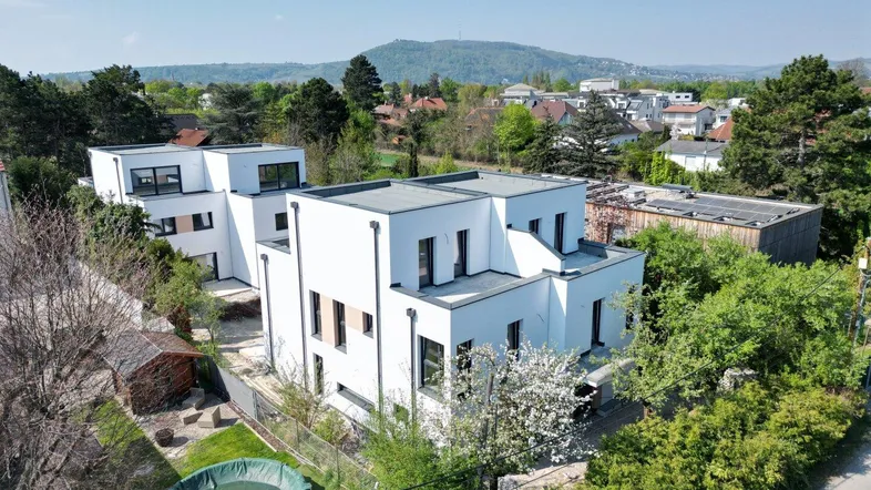 Luftaufnahme von zwei modernen weißen Gebäuden mit Flachdächern in einer grünen Umgebung.