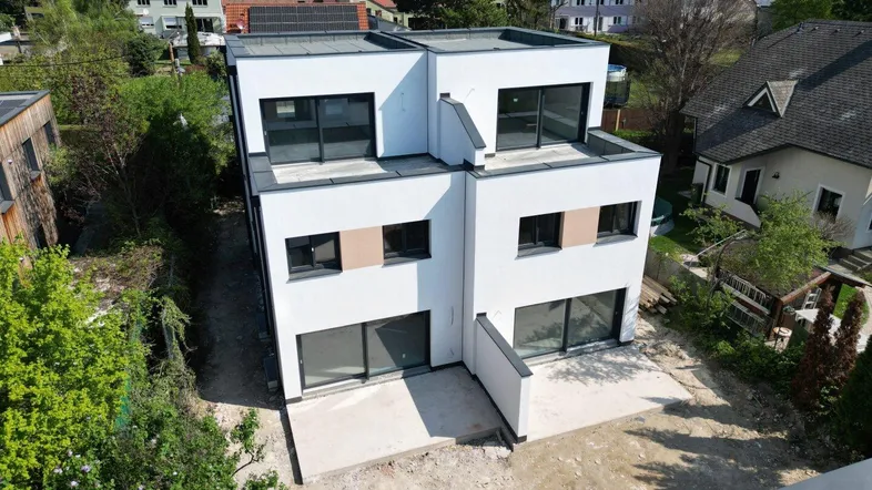 Moderne Doppelhaushälfte mit Flachdach und großen Fensterfronten in grüner Umgebung.