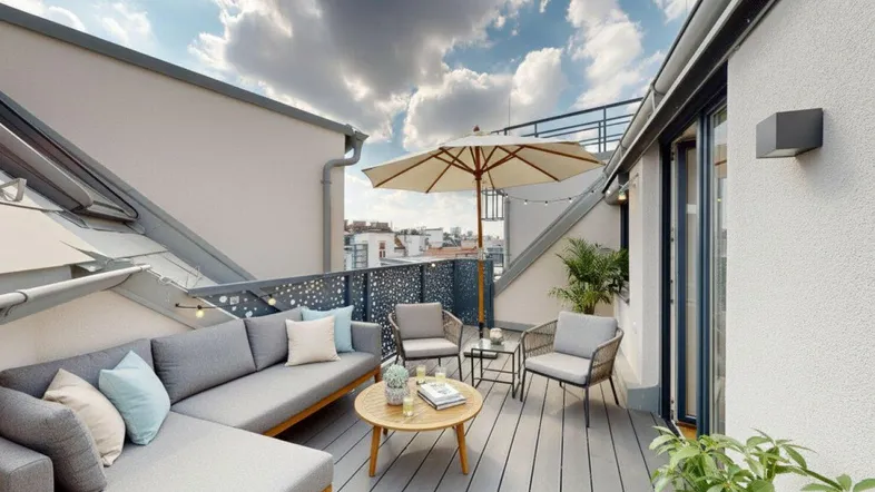 Möblierte Dachterrasse mit bequemen Sitzgelegenheiten, Sonnenschirm und Blick über die Stadt.